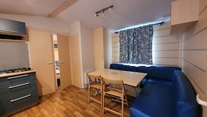 A compact kitchen with a gas stove, a dining table with chairs, and a blue sofa. - MobileHome VERONA, air-conditioned, TV, WIFI, 15 min from Europa-Park! (Boofzheim)