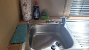 A stainless steel sink with a chrome faucet, a roll of toilet paper, a bottle of dish soap, and a green sponge. - MobileHome VERONA, air-conditioned, TV, WIFI, 15 min from Europa-Park! (Boofzheim)