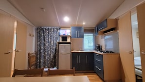 A compact kitchen with a refrigerator, microwave, stove, and sink. There is a dining table with chairs. - MobileHome VERONA, air-conditioned, TV, WIFI, 15 min from Europa-Park! (Boofzheim)