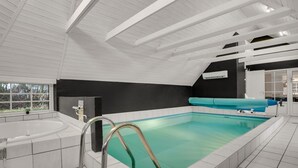 Una piscina interior moderna con vista despejada a la estructura del techo, un área de bañera separada y un ventanal que ofrece vistas al exterior.