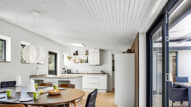 Une cuisine moderne avec des meubles blancs, une table à manger en bois et une porte vitrée donnant sur un espace extérieur.