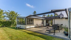 Une maison moderne dotée d’un patio couvert, d’un espace barbecue et d’une pelouse bien entretenue.