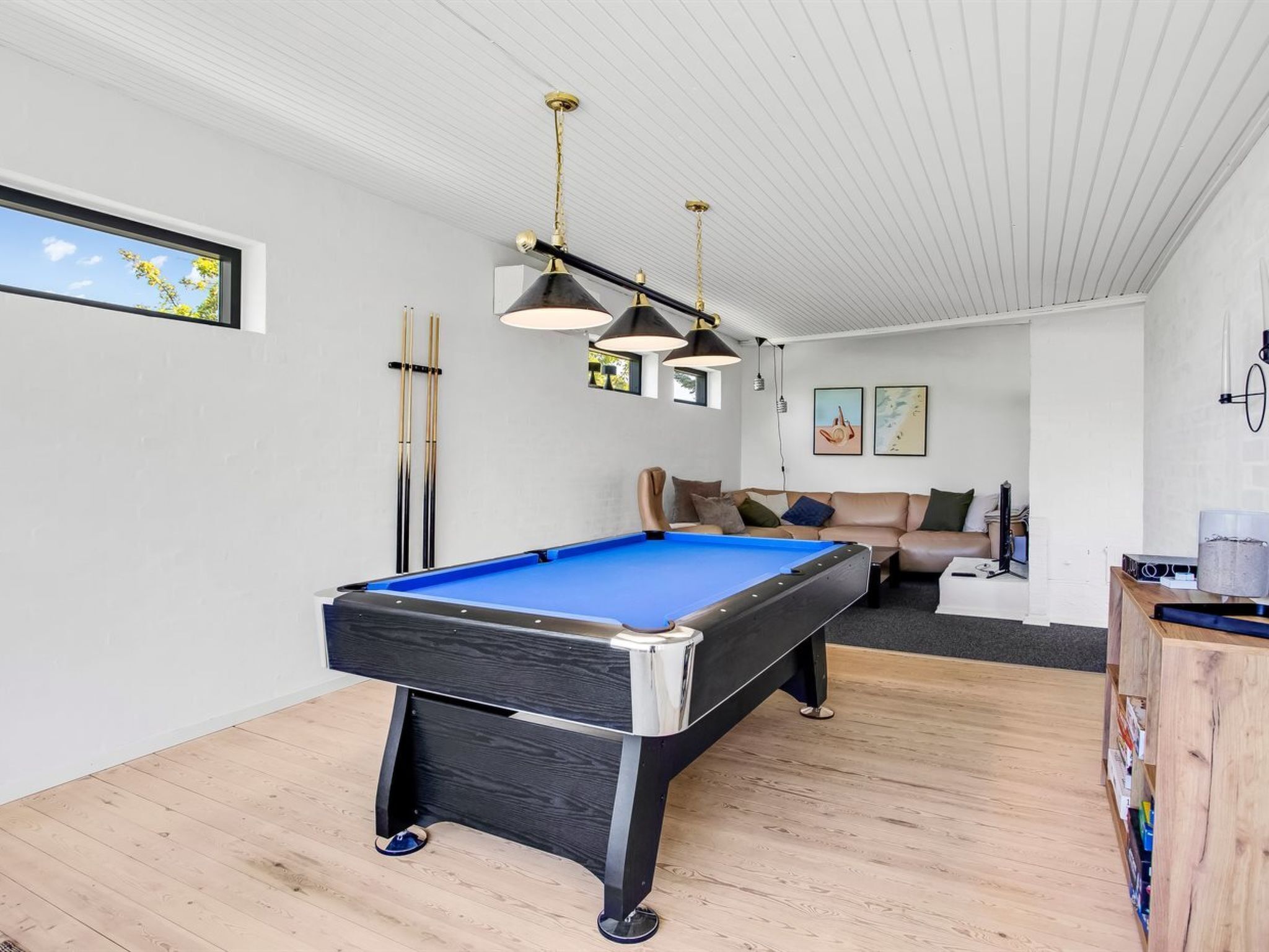 Een pooltafel in een kamer met een houten vloer, een bank en een plafond met een rasterpatroon.