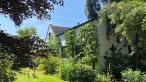 A house with a sloped roof, surrounded by lush greenery and trees.
