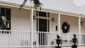 A white building with a covered porch, a black wreath, and two black planters. - The Notebook Haus in Omeo (Omeo)