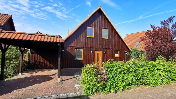 A wooden house with a sloped roof, a front porch, and a well-maintained garden.