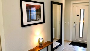 A hallway with a framed picture, a mirror, a floor lamp, and a door.