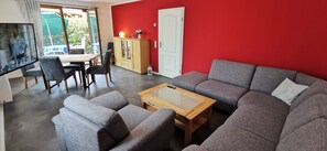 Una sala de estar con pared roja, sofá gris, mesa de centro de madera y un área de comedor con una mesa y sillas.