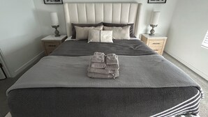 A neatly made bed with a grey and white striped blanket, two bedside tables with lamps, and two framed floral wall art pieces.