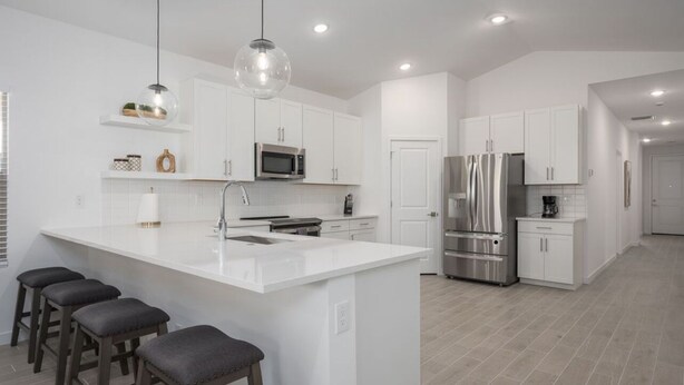 A modern kitchen with white cabinetry, stainless steel appliances, and a central island with bar stools.