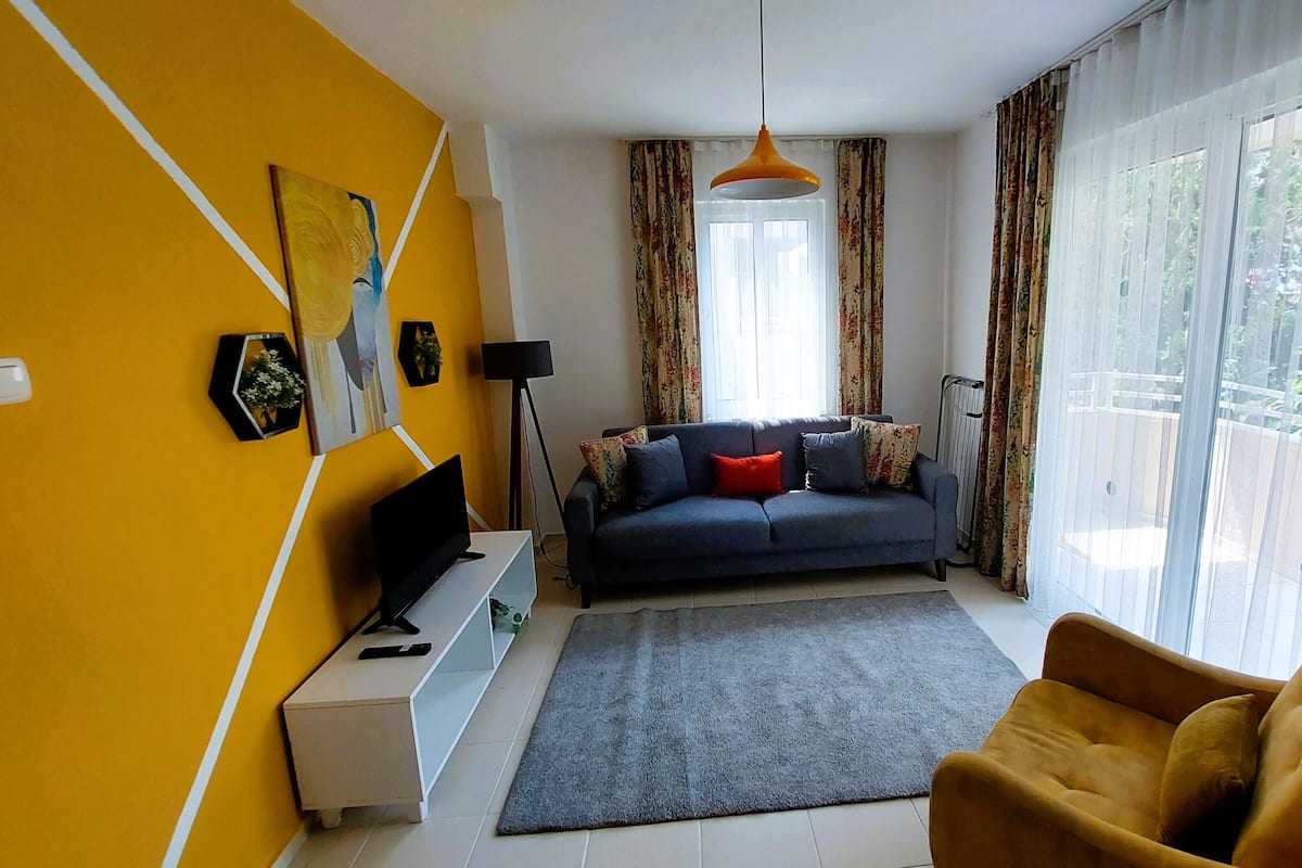 Een woonkamer met een bank, een televisie, een salontafel en een gele fauteuil.
