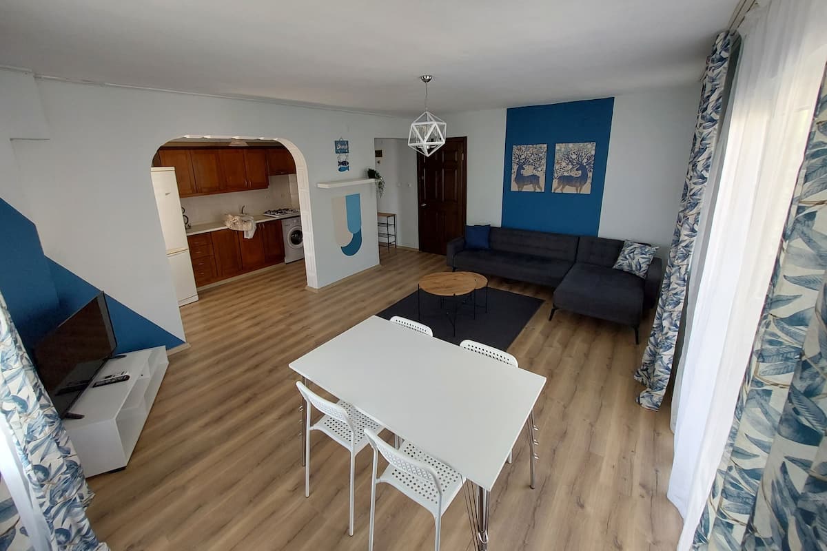 Een moderne woonkamer met een bank, een eettafel en een keuken, zichtbaar door een boog.