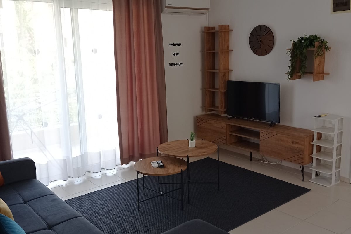 Een moderne woonkamer met een donkerblauwe bank, een salontafel, een televisie en een houten kast.