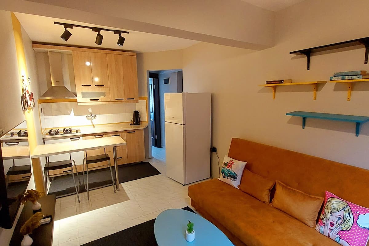 Een compacte woonruimte met een kitchenette, een bank, een salontafel en een eethoek.