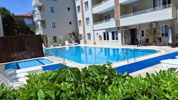 A swimming pool with lounge chairs, a fenced area, and a building with balconies and windows.