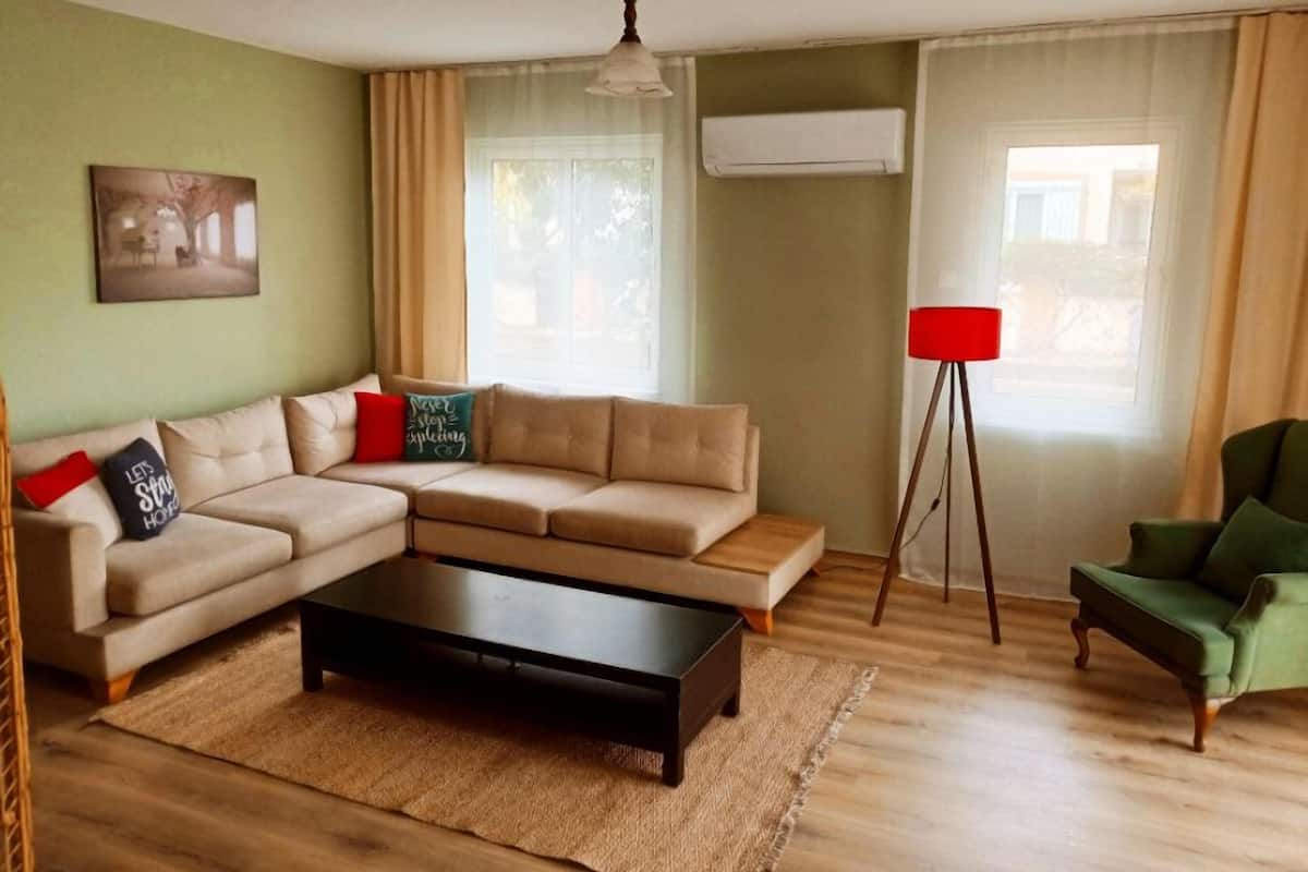 Een woonkamer met een modulaire bank, een salontafel, een vloerlamp en een groene fauteuil.