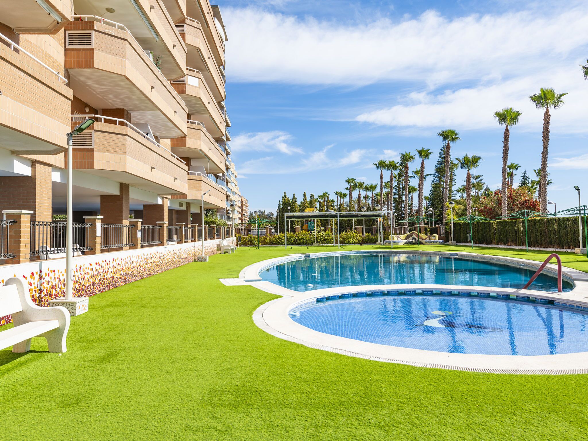 A swimming pool surrounded by a well-maintained lawn, with a multi-story building in the background.