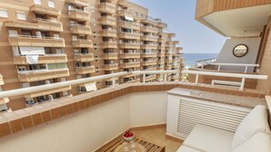 A balcony with a wooden table, white sofa, and a view of a high-rise building with balconies.