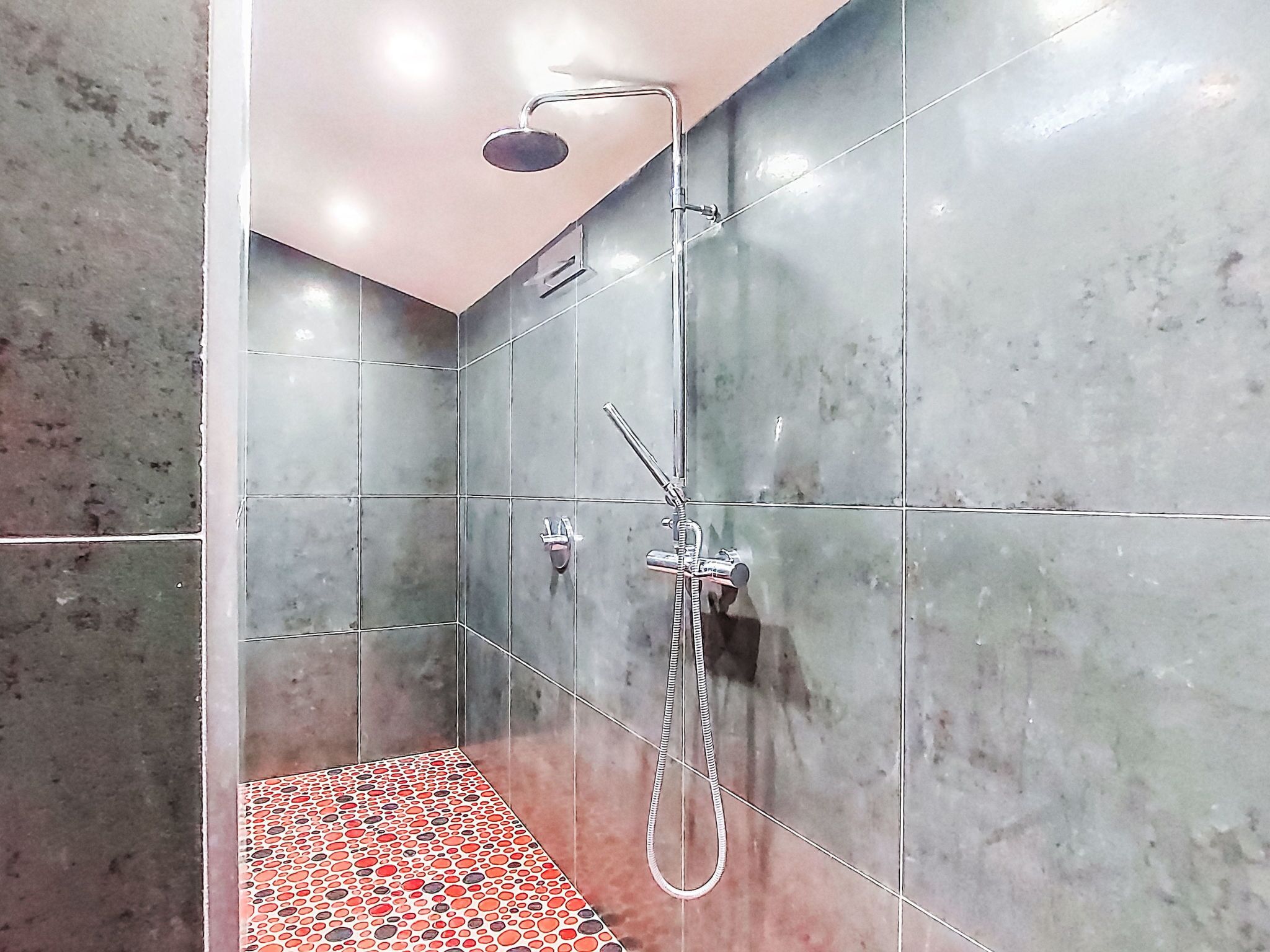 A modern shower area with a handheld showerhead, a fixed showerhead, and a handheld shower hose.