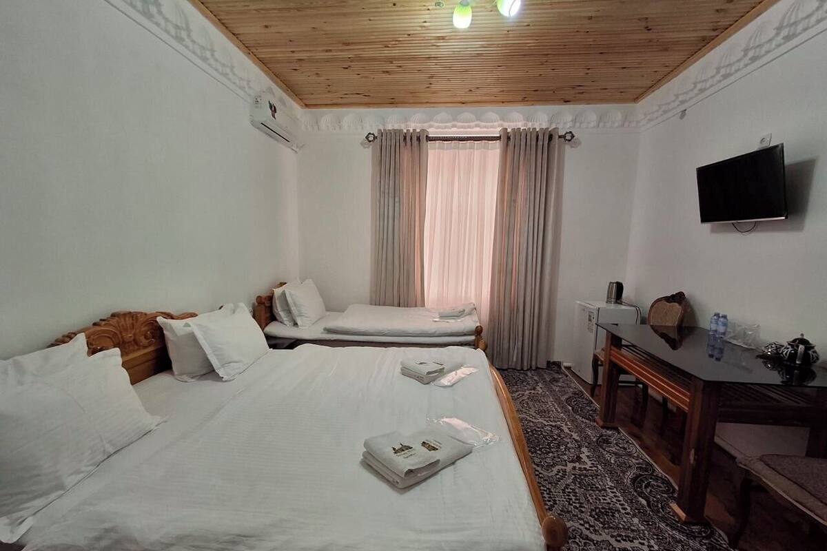 A hotel room with two beds, a desk, a television, and a window with curtains.