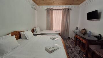 A hotel room with two beds, a desk, a television, and a window with curtains.