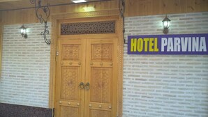Entrada de un hotel con un gran puerta doble de madera, un cartel que dice "HOTEL PARVINA" y dos faroles de pared.