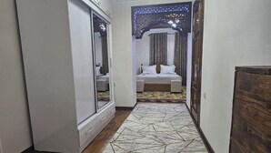 Un estrecho pasillo con piso de madera, una alfombra de diseño geométrico, una cama con dosel y un candelabro.