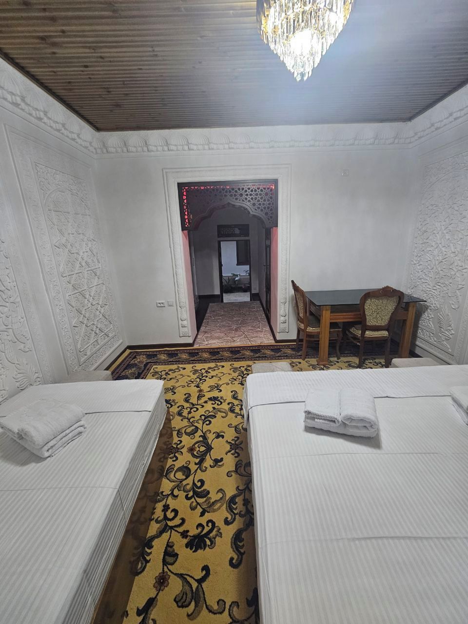 A hotel room with two beds, a dining table, and a chandelier.