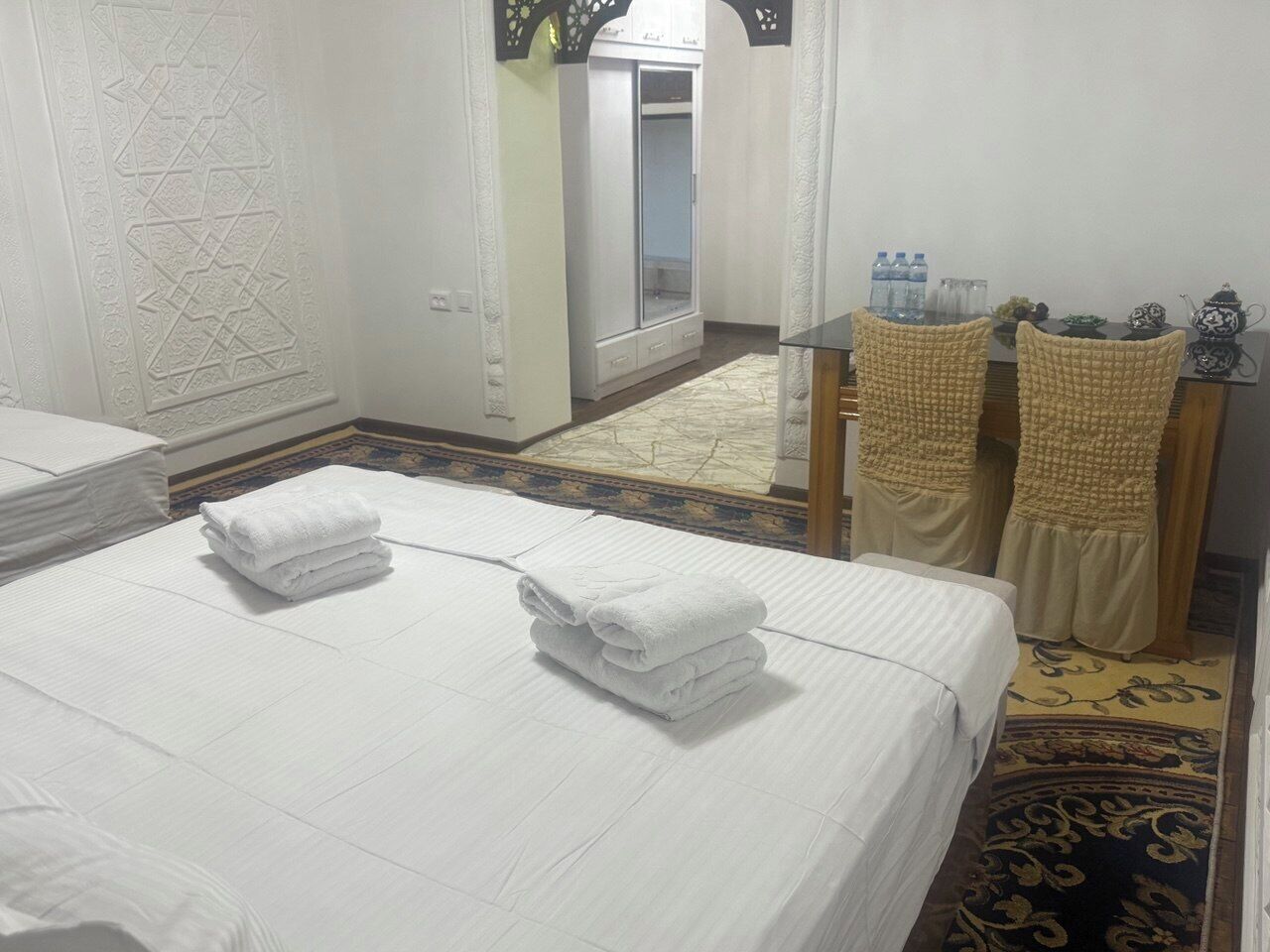 A hotel room with two beds, a sitting area with a table and chairs, and a wardrobe.