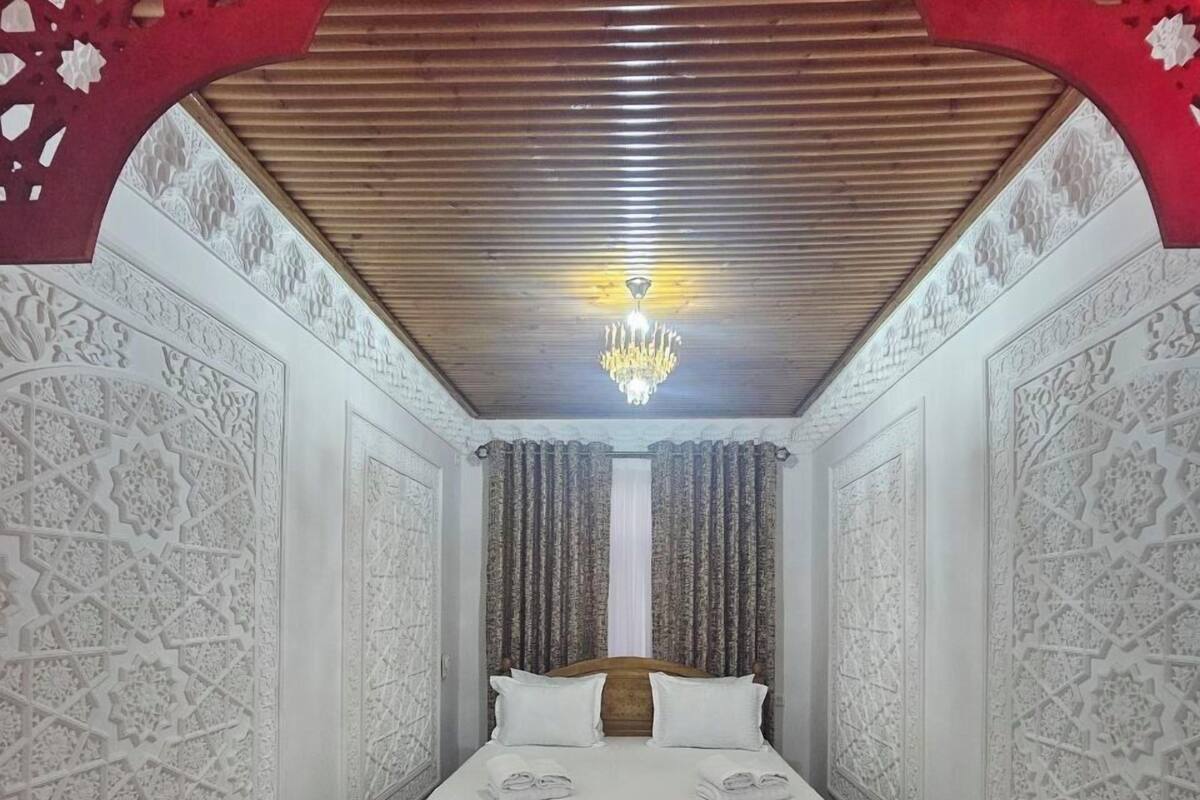 A bedroom with a bed, a chandelier, marble flooring, and intricate wall designs.