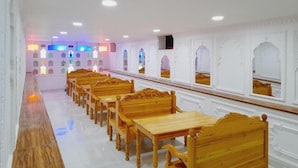 Un largo pasillo con filas de bancos y mesas de madera, paredes blancas con molduras decorativas e iluminación empotrada.