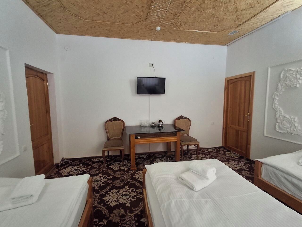 A room with two beds, a table with chairs, a television, and a patterned carpet.