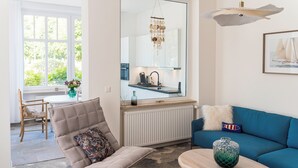 Un salon moderne comprenant un canapé, un fauteuil, une table basse et donnant sur la cuisine.