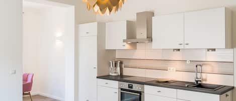 A modern kitchen with white cabinetry, a built-in oven, a stainless steel sink, and a unique pendant light.