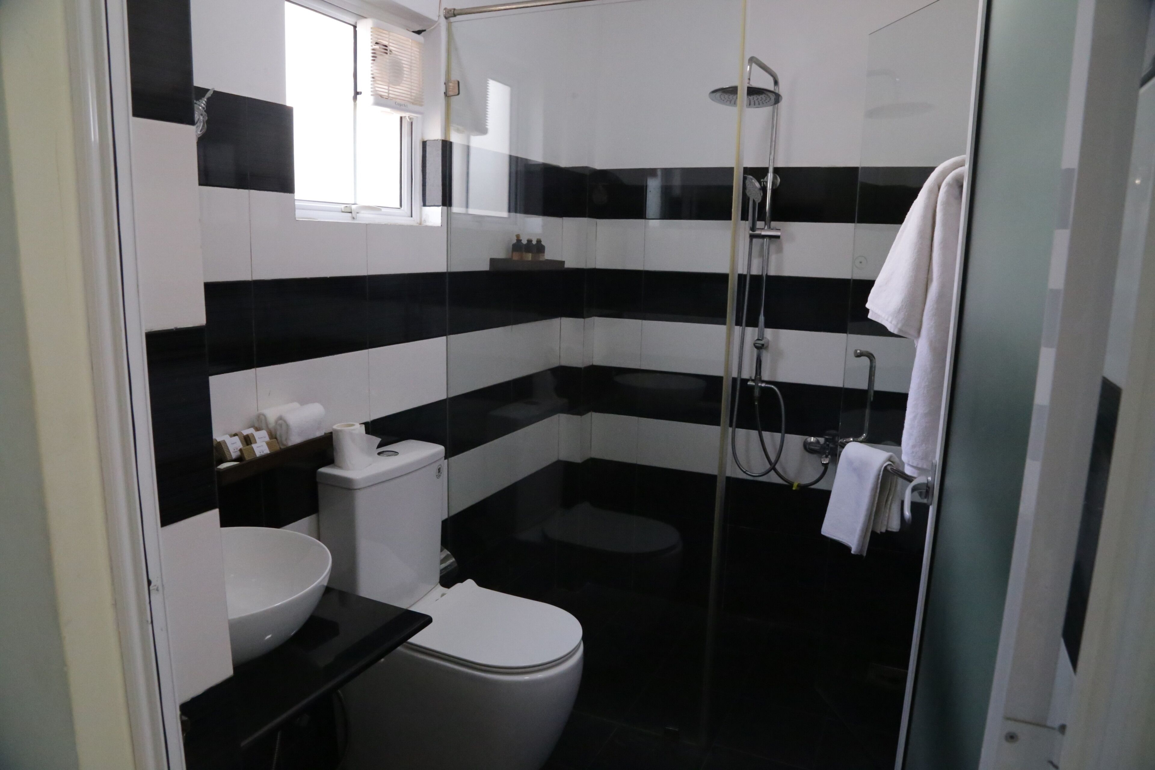 A bathroom with a black and white tiled wall, a white sink, a toilet, and a glass-enclosed shower area.