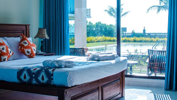 Une chambre d’hôtel avec un grand lit, une vue sur la piscine et un balcon avec des chaises.