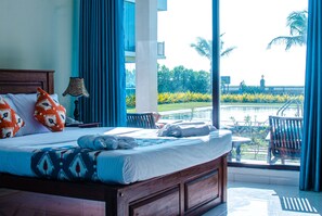 Une chambre d’hôtel avec un grand lit, une vue sur la piscine et un balcon avec des chaises.