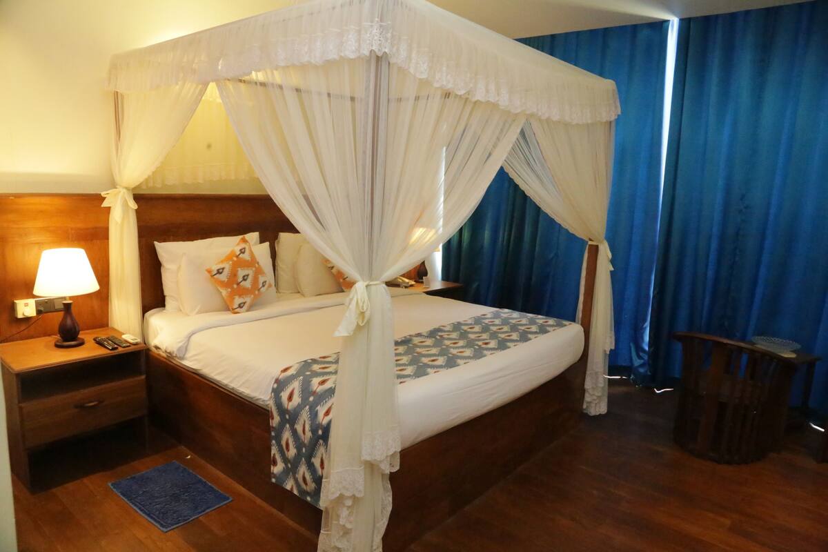 A four-poster bed with a canopy, a bedside table with a lamp, and a small trash bin.