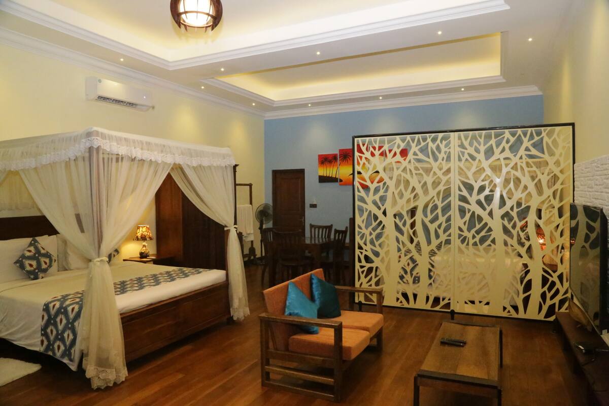 A hotel room with a bed, a chair, a table, and a decorative partition.