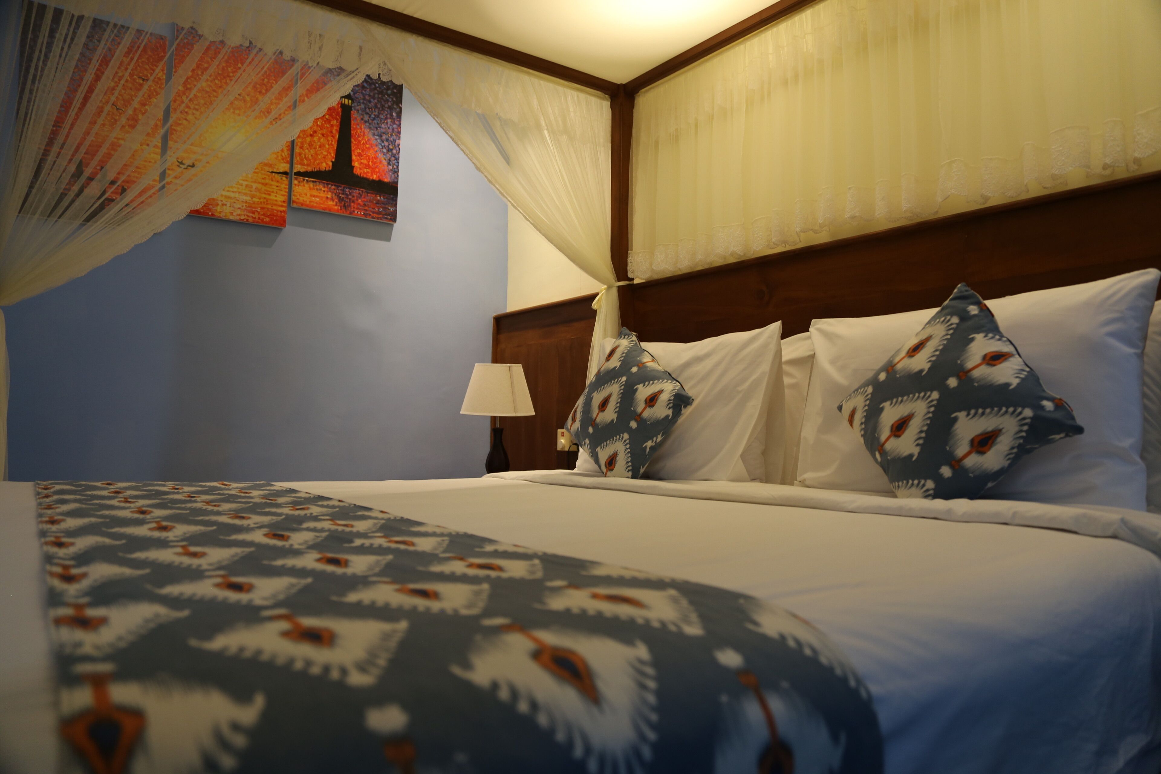 Quarto de hotel com cama, mesa de cabeceira, luminária e um quadro na parede.