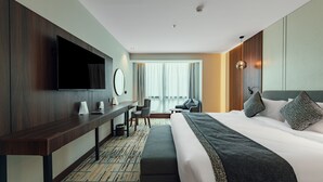 Ein modernes Hotelzimmer mit einem großen Bett, einem Schreibtisch, einem flachbildfernseher an der Wand und einem großen Fenster mit Vorhängen.