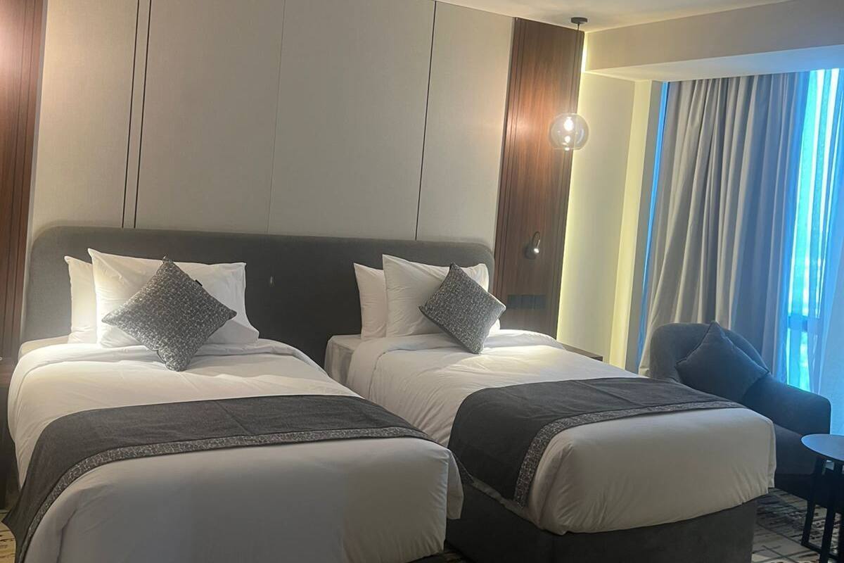 A hotel room with two beds, a small table, and a window with curtains.