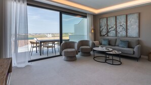 A modern living room with a large sliding glass door leading to an outdoor terrace. There are two armchairs, a sofa, and a coffee table. A painting is on the wall, and a lamp is on the side table.