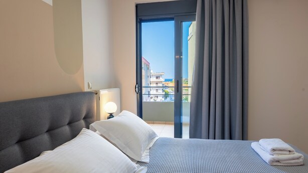 Une chambre d’hôtel avec un lit, des oreillers, une lampe, un balcon avec des rideaux et une vue sur les bâtiments.
