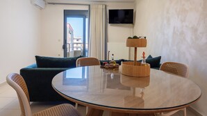 Un salon moderne avec une table ronde en verre, deux canapés, un téléviseur fixé au mur et une vue sur le balcon.