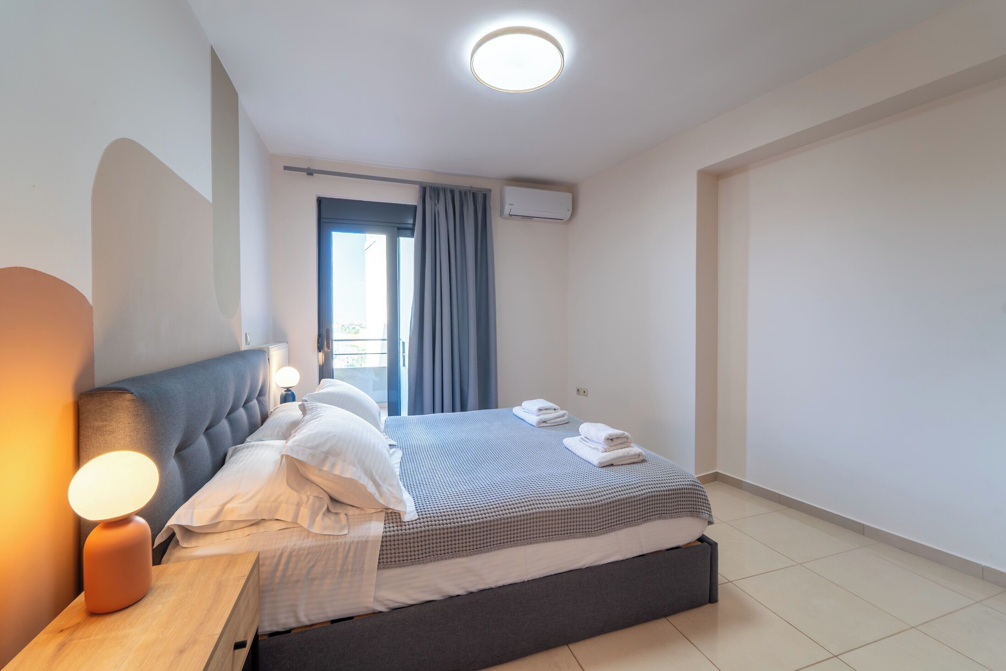 A modern bedroom with a bed, bedside lamp, and an air conditioning unit.