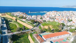 Vue aérienne d’une ville côtière dotée d’un rempart, d’un terrain de basketball et d’un phare visible au loin.