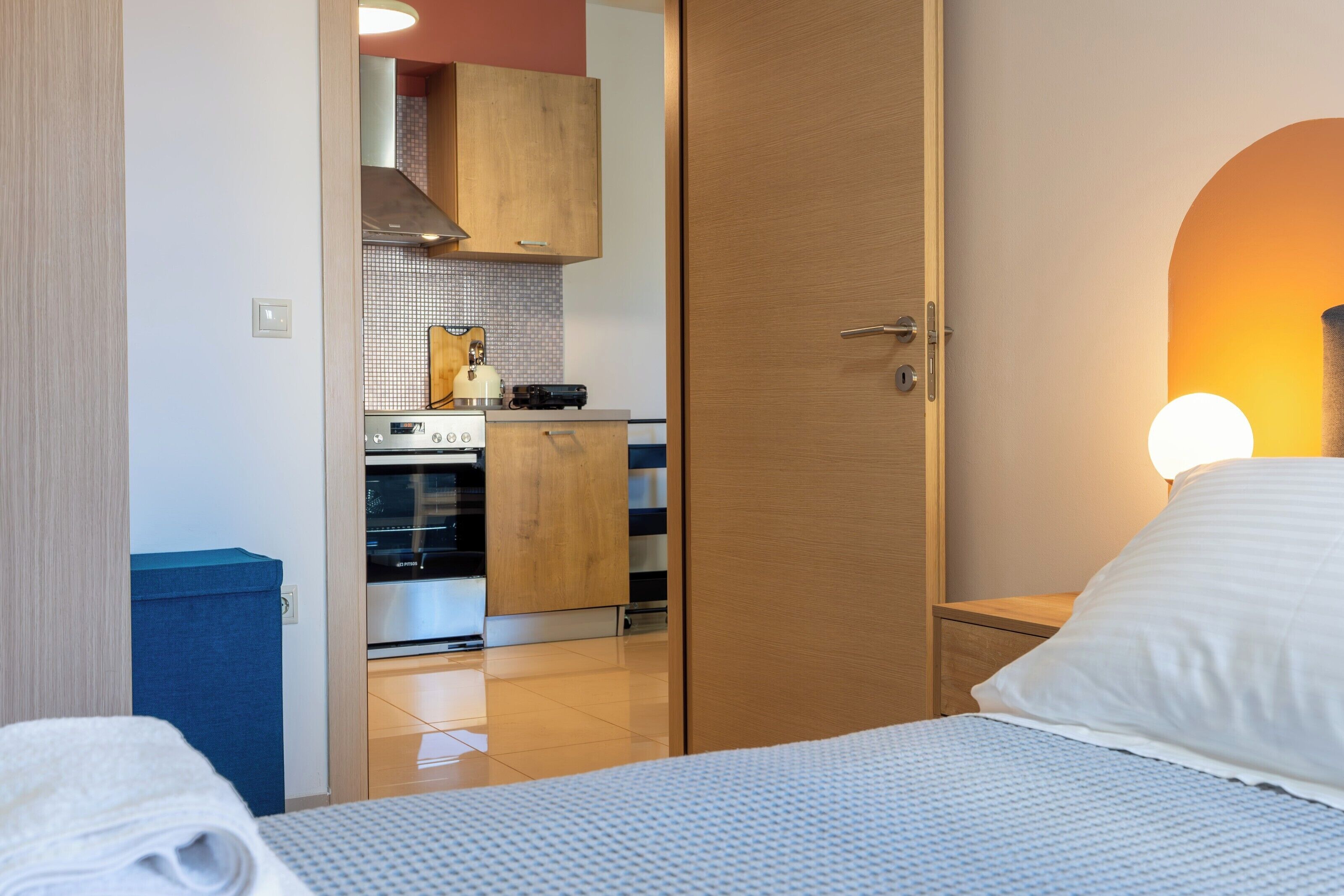 A hotel room with a bed, a nightstand, a wooden wardrobe, a kitchenette, and a bathroom.