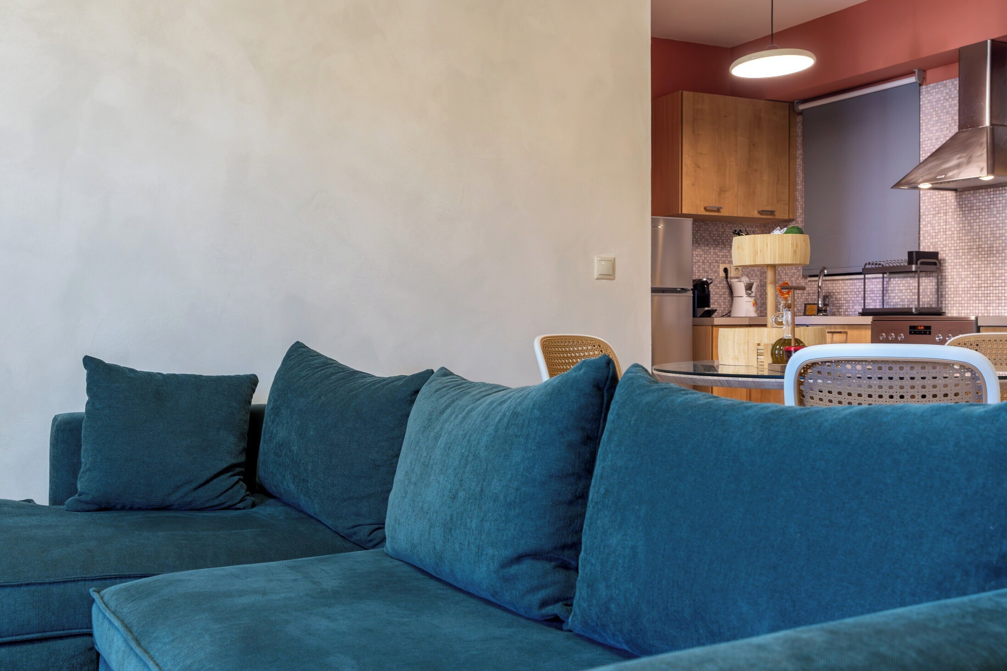Una sala de estar moderna con un sofá color turquesa, una mesa de comedor con sillas y una zona de cocina con armarios de madera y una estufa.