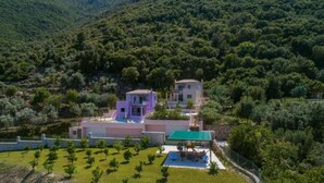 Una villa moderna con piscina, rodeada de exuberante vegetación y colinas.